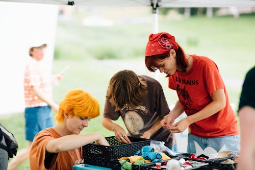 A group of adults look through art making supplies under a large event tent while outside on a sunny summer day.