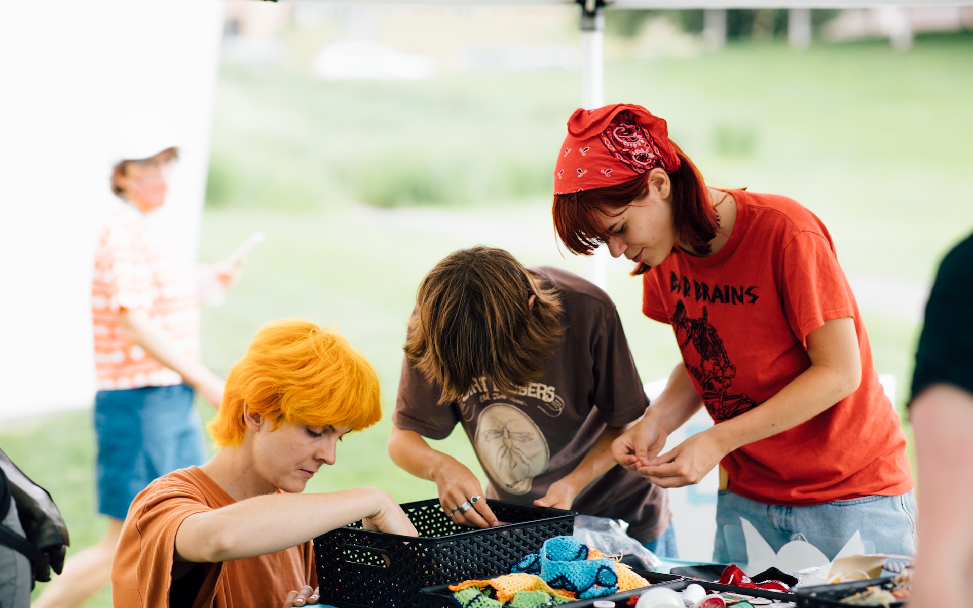 A group of adults look through art making supplies under a large event tent while outside on a sunny summer day.