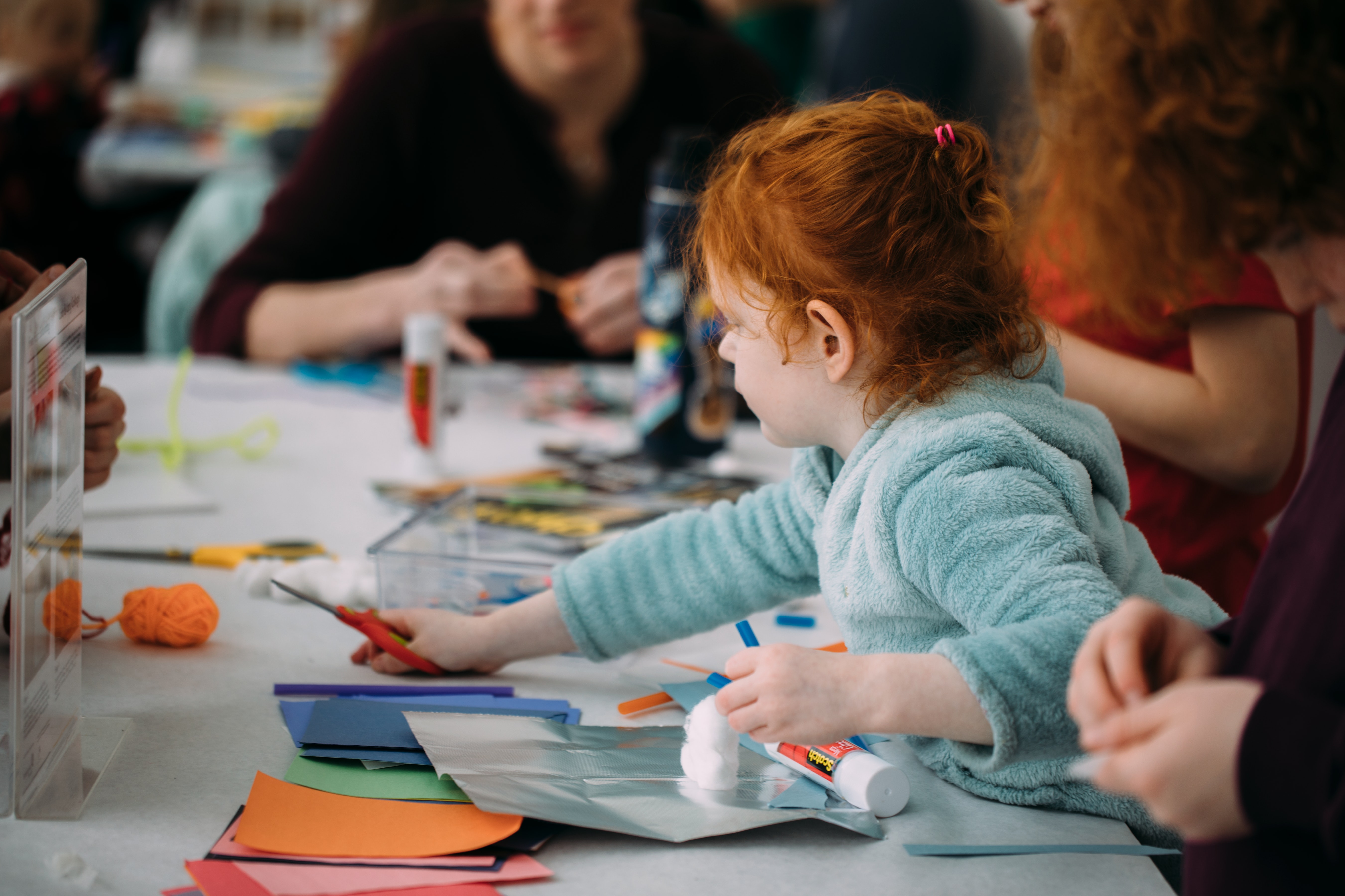 A child with light skin makes art using paper and scissors at a table.