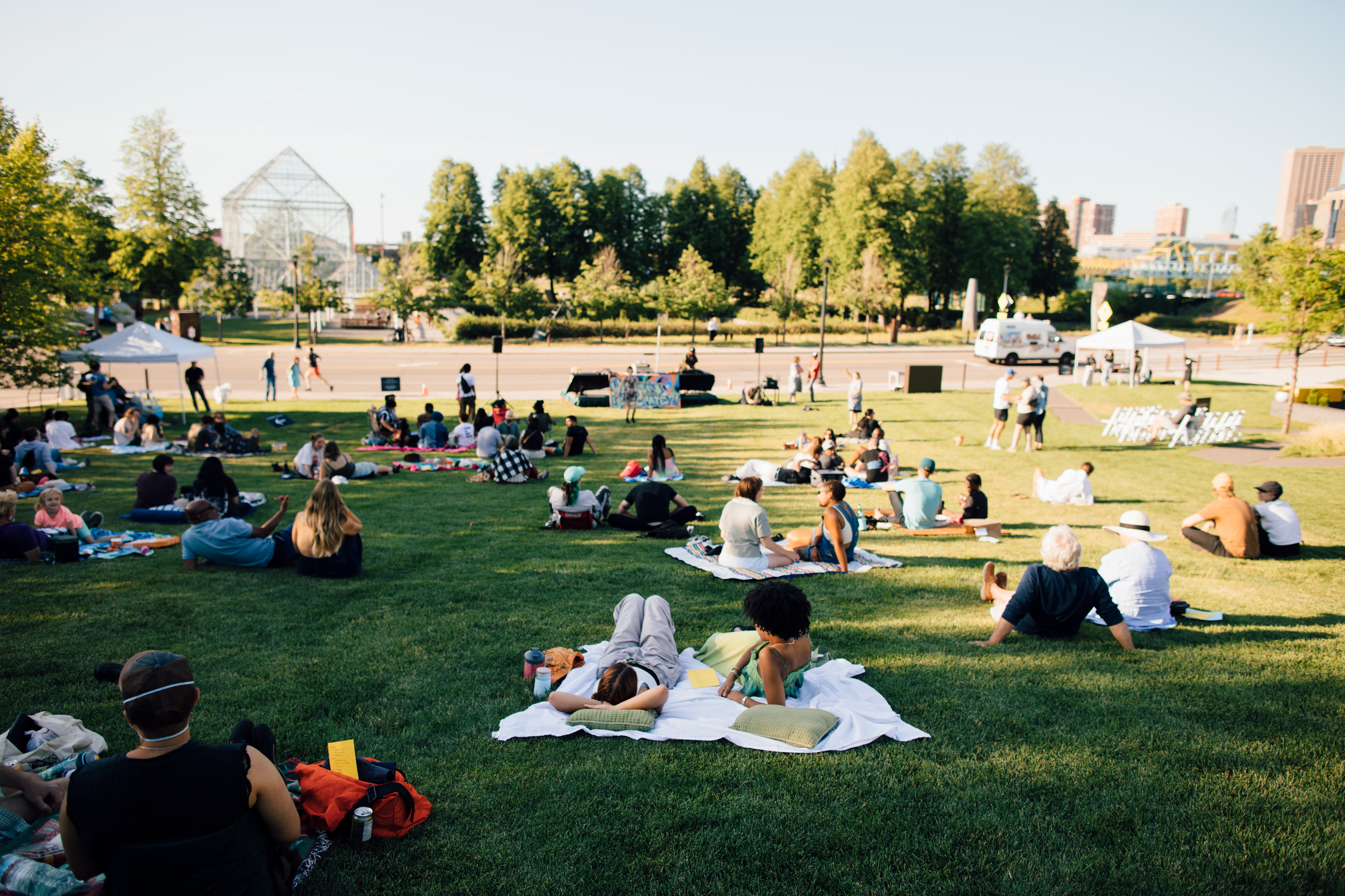Small groups of people lying on blankets on a grassy lawn under a sunny day.