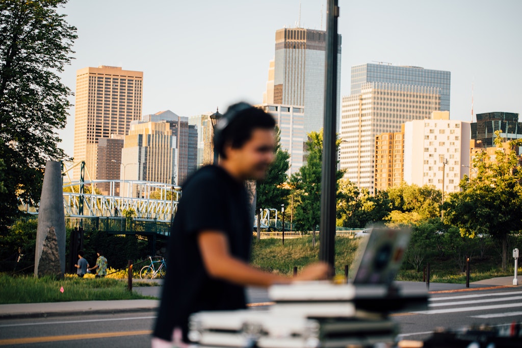 A person using DJ equipment outdoors with a city skyline in the background.