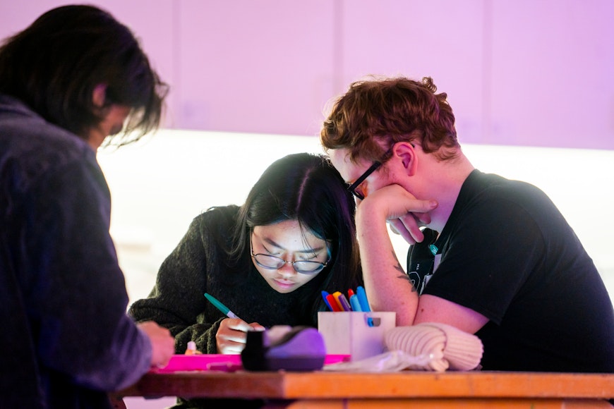 Three adults stare down at the artwork they are making while sitting at a table together.
