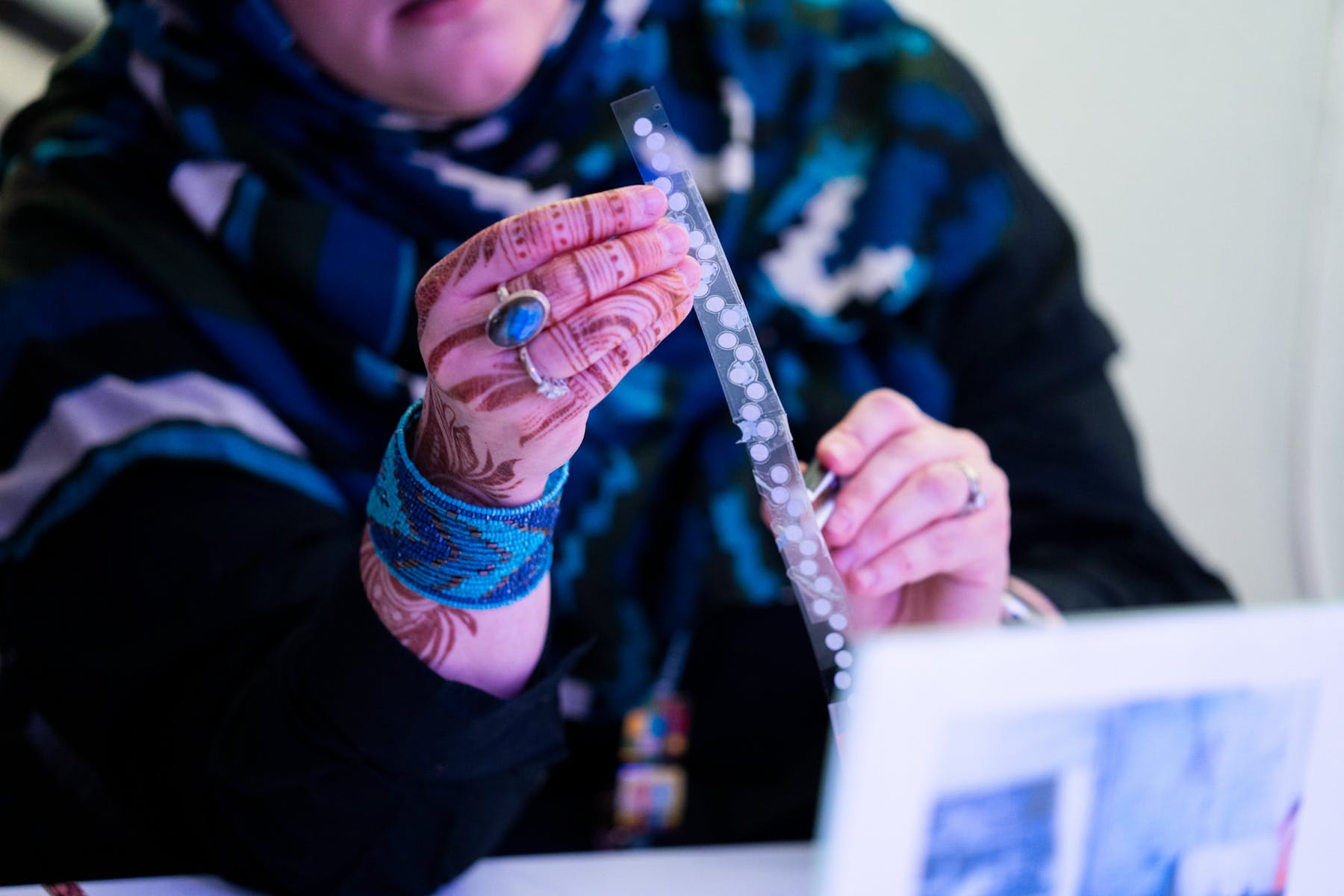 Hands with henna ink patterns holds up a translucent trip with white dots on it.