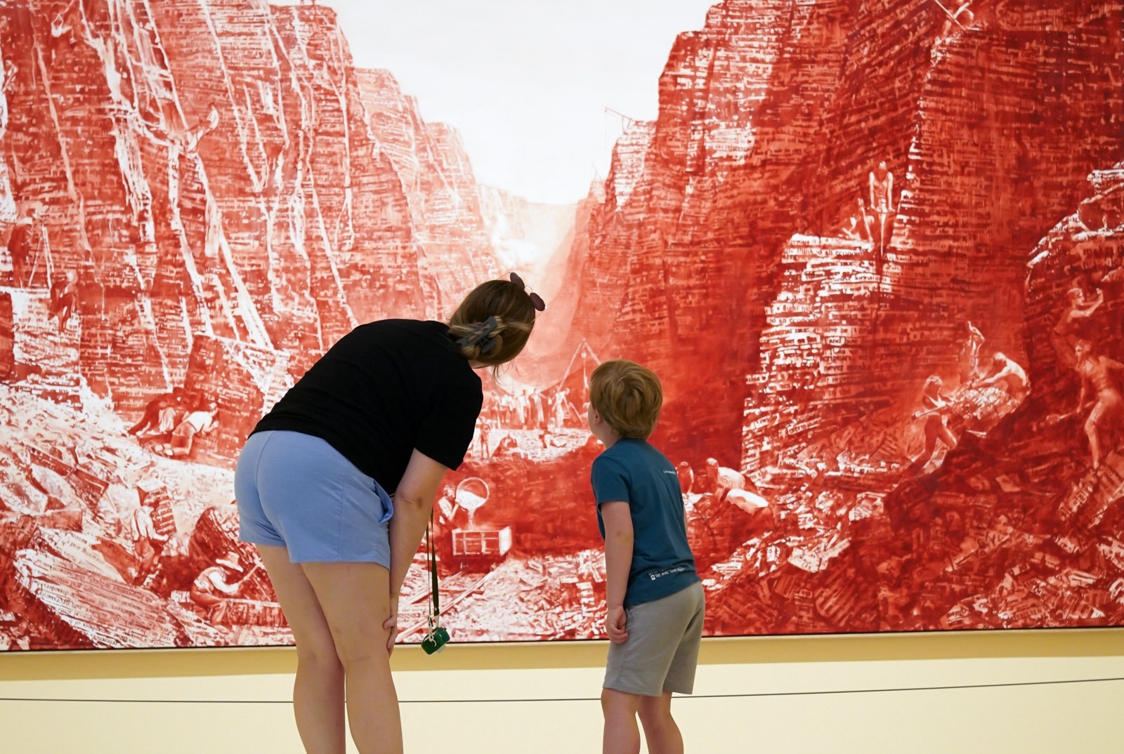 A woman and child view a large red-toned canyon artwork in a gallery.