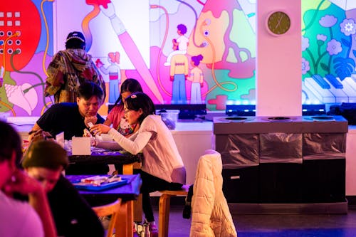A group of three adults sit at a table and work on artwork together.