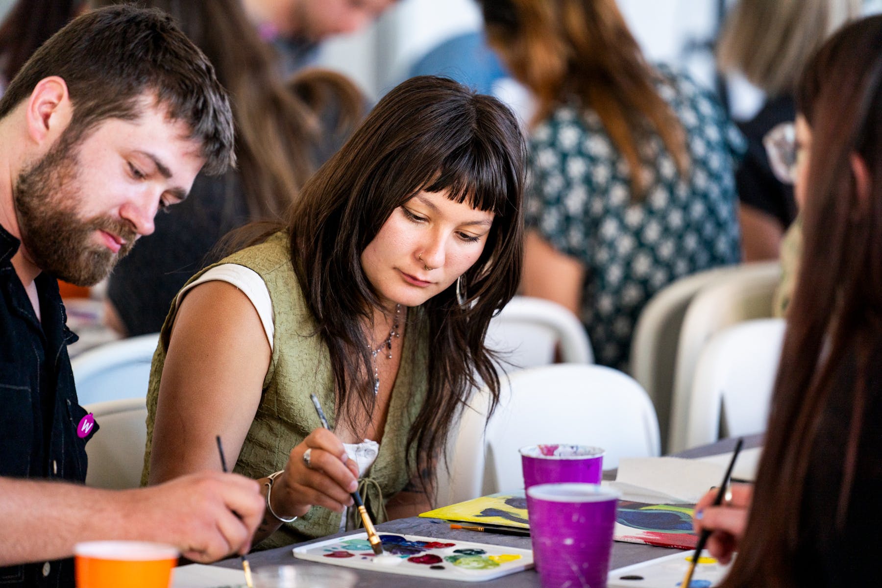 Two adults dab brushes in pain while seated next to one another at a table.