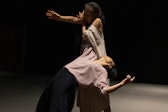 One performer with medium skin leans backward, one arm supported by another performer.