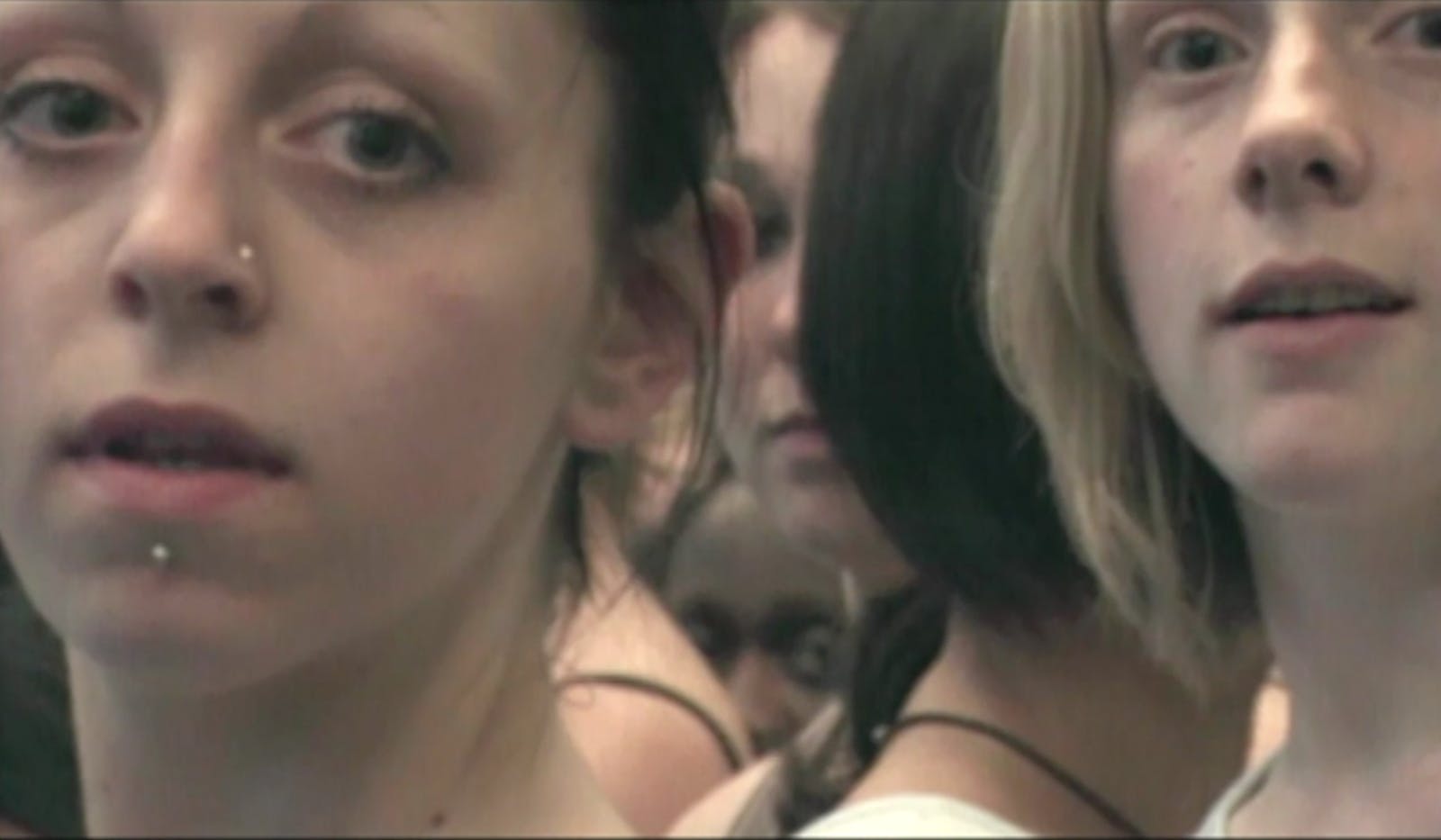 Faces of multiple dancers fill the image as they stand together closely and stare ahead, appearing to glance at the viewer.