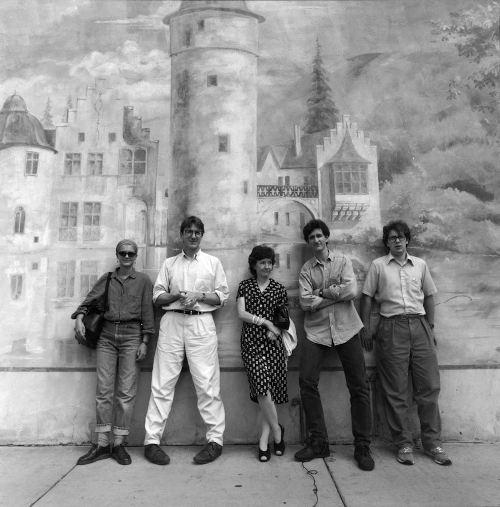 Four adults stand against a wall that has a castle painted on it.