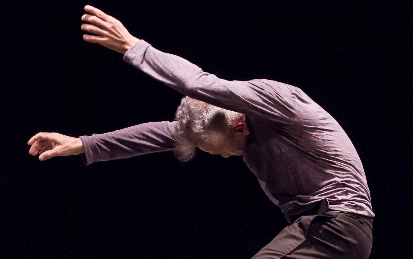A man in a dress shirt leans forward with his arms out while dancing.