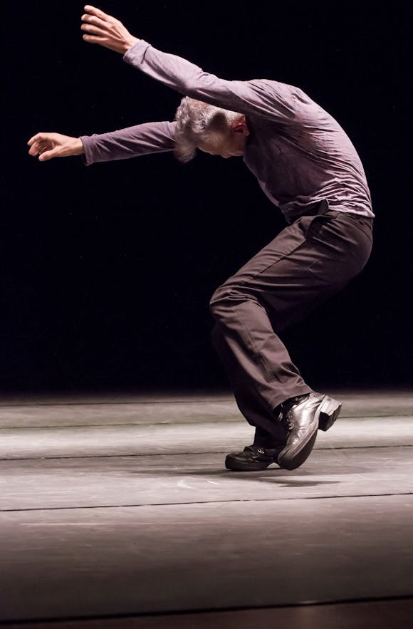 A man dances on stage wearing a dress shirt and slacks.