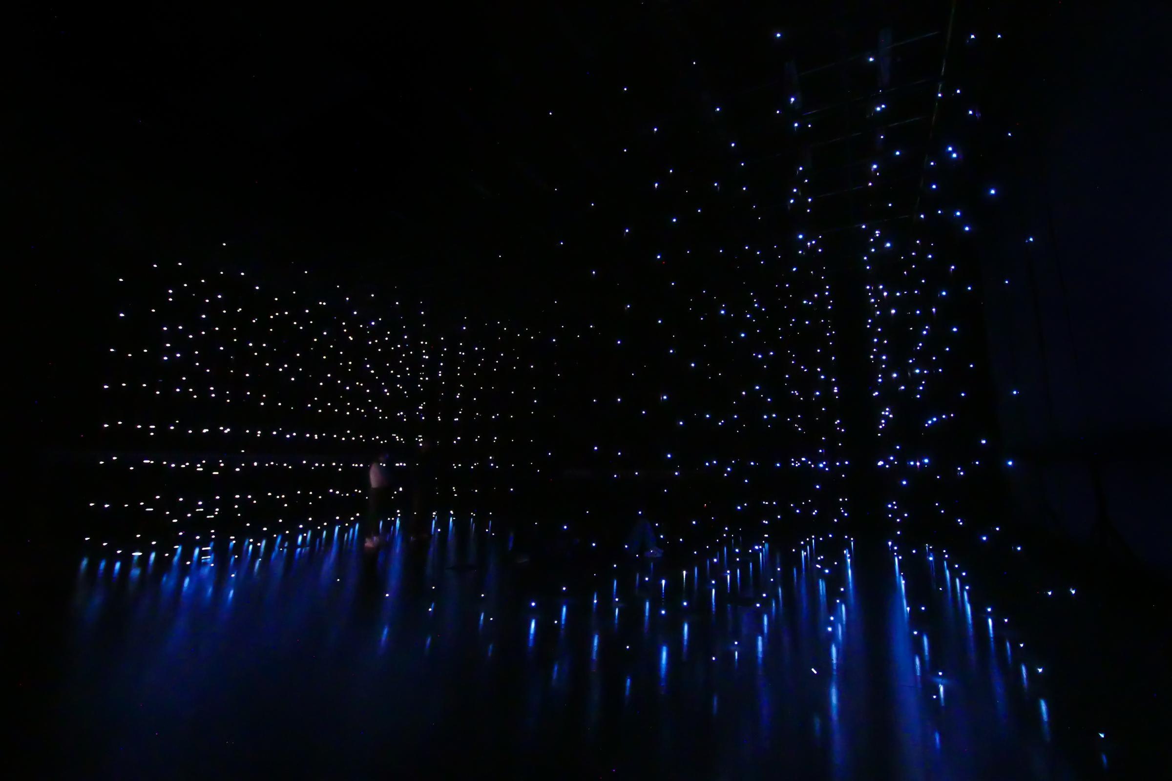 Glowing dots in a grid hang in a darkened space.