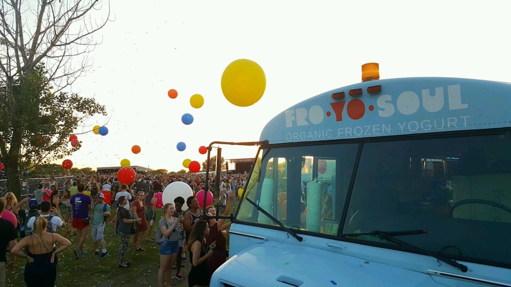 Crowd at an outdoor festival with colorful balloons and a frozen yogurt truck labeled Fro Yo Soul.