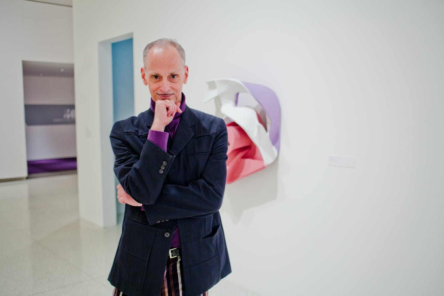 A man stands with his arms crossed and a hand to his chin while smiling at the viewer.