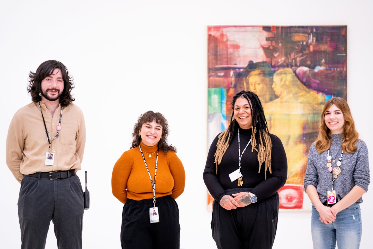 A group of adults smile at the viewer while standing in front of a painting in an art gallery.