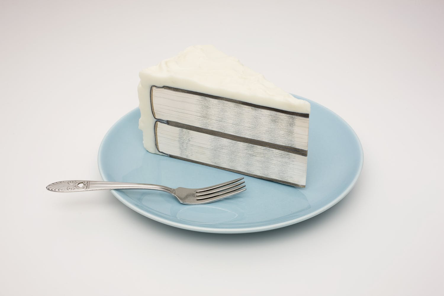 A book that appears to be a slide of cake sits on a plate with a fork.