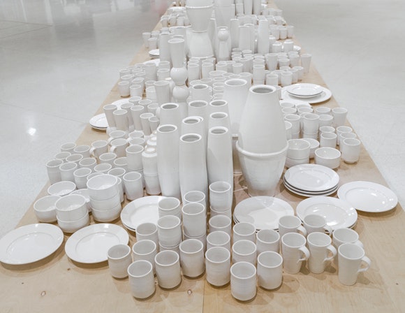 A variety of white cermaic cups, plates, bowls, and vases are collected on a wooden table.