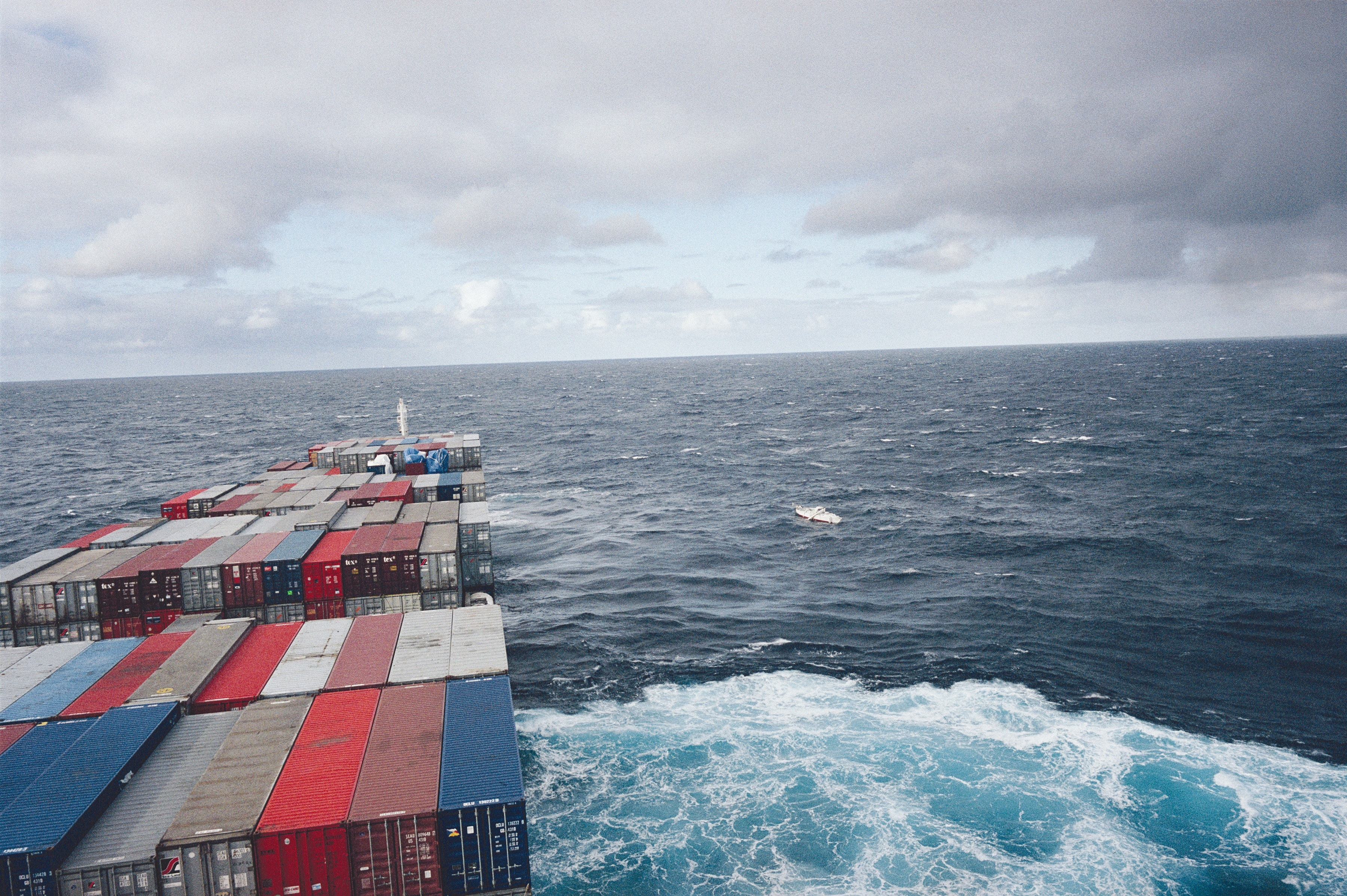 A large boat carrying many shipping containers sails across a large, blue ocean.