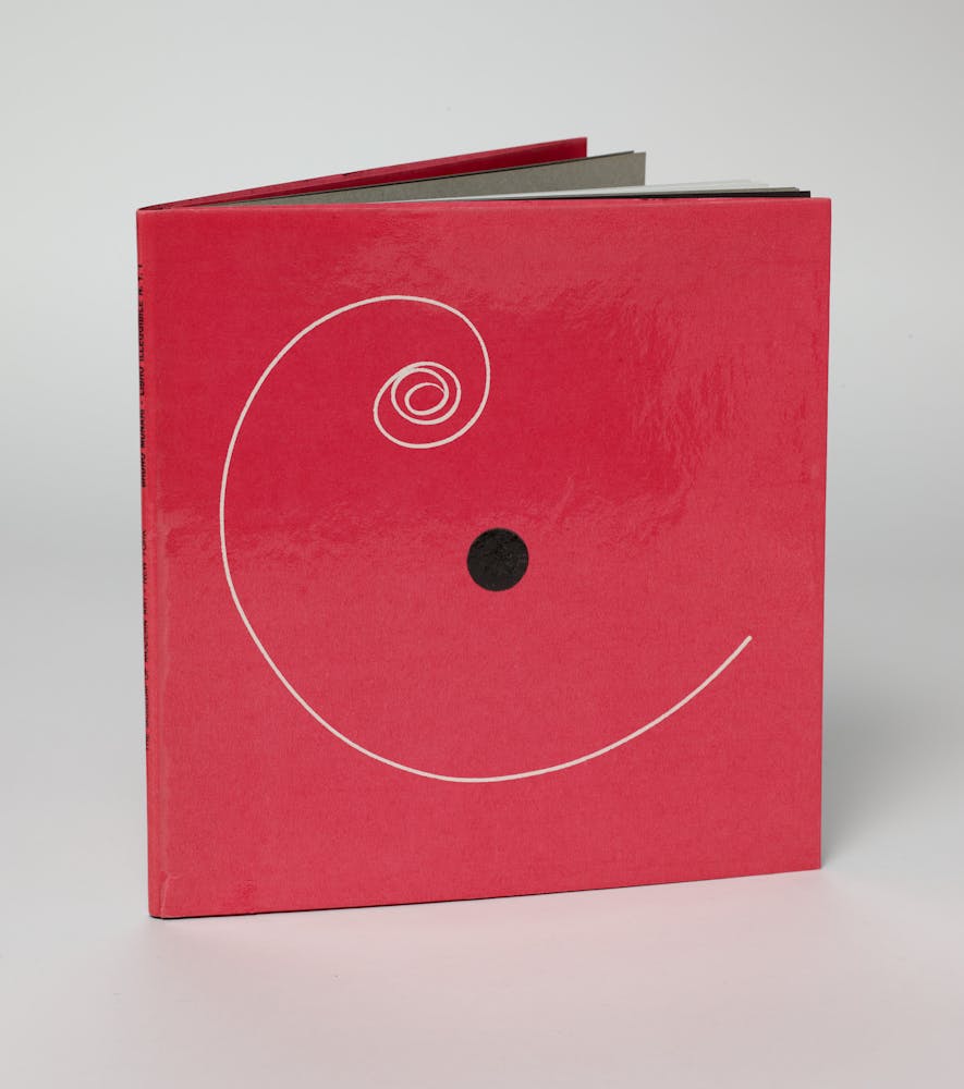 A square red book with a white spiral and black dot on the cover.