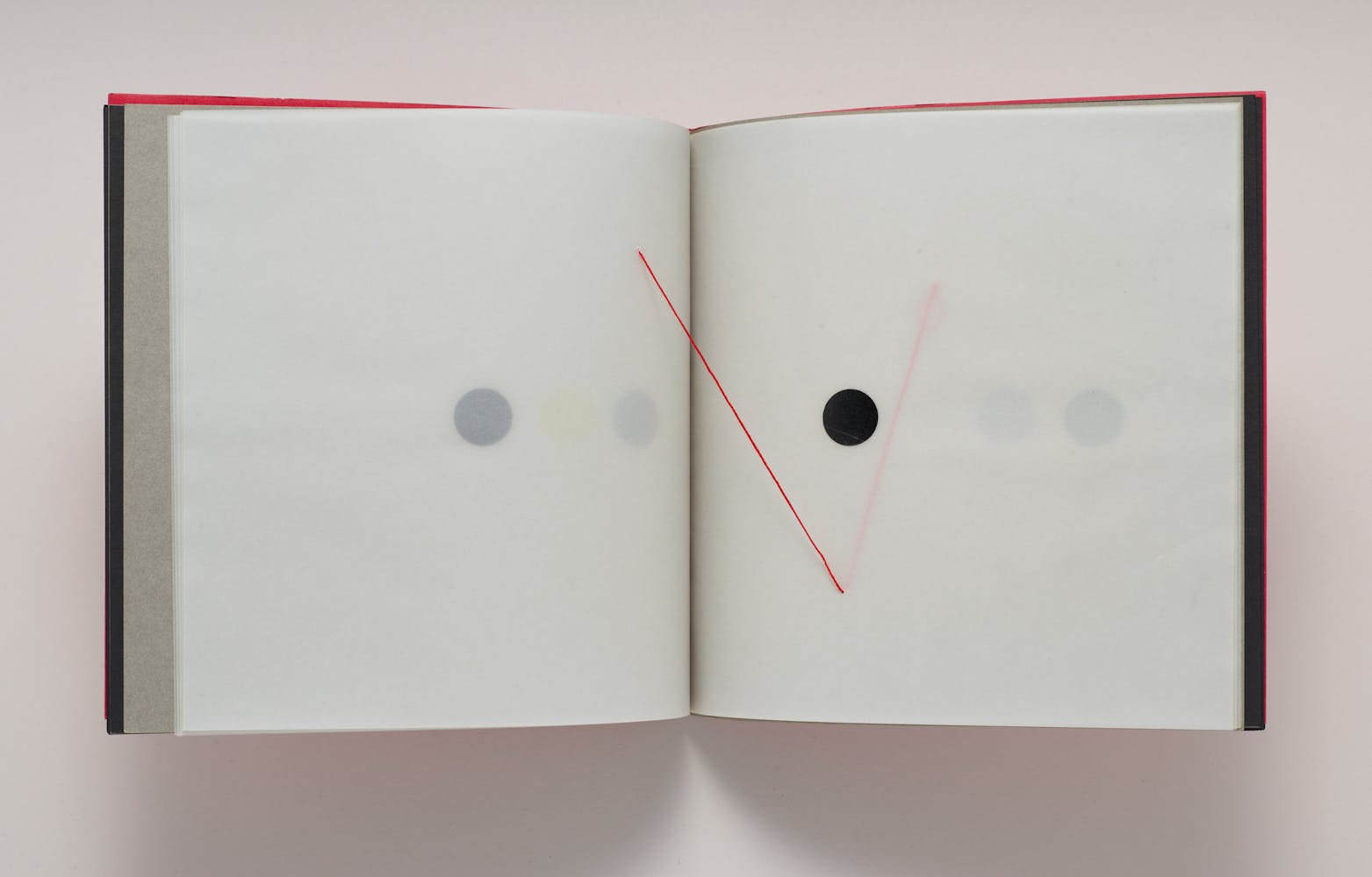 A book is opened to a spread with a black dot and a red string running through multiple pages.