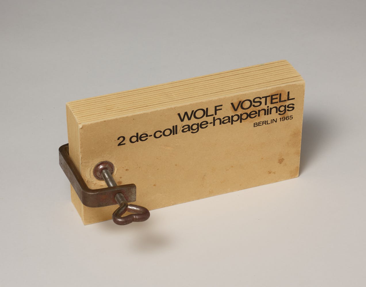 A book made from two pieces of plywood held together with a metal clamp sits on a tabletop.