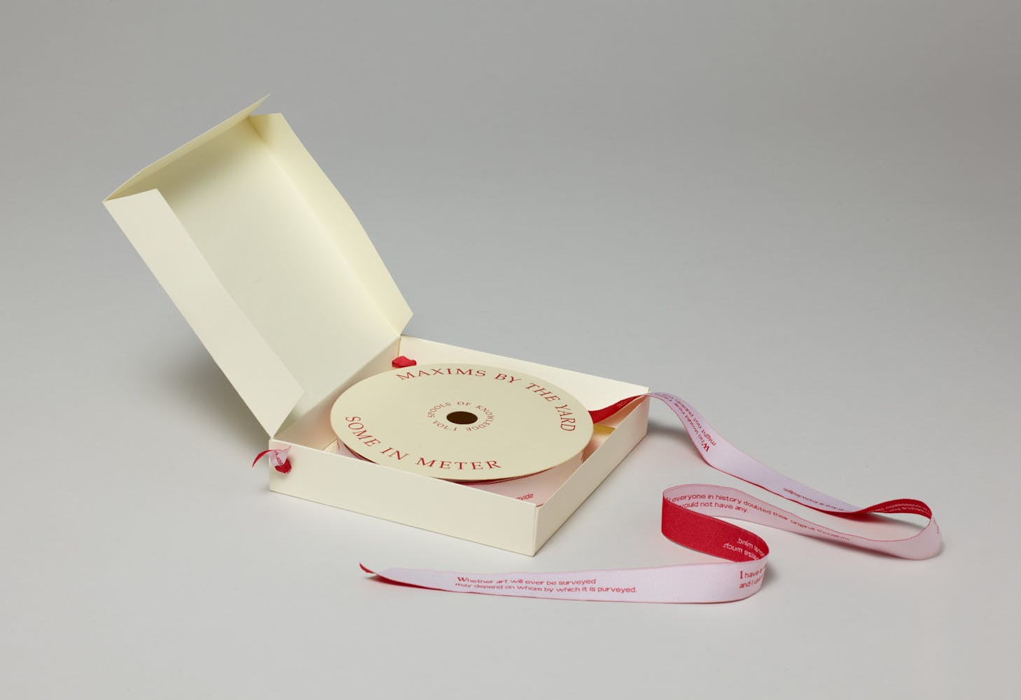 Book made of a spool of ribbon with writtings printed on it sits inside a paper box.