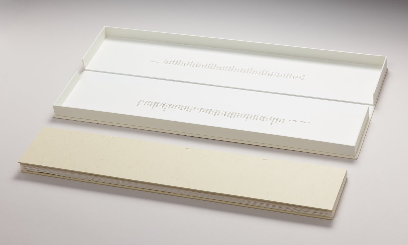 A long thing white book sits next to a a box that it fits inside of.