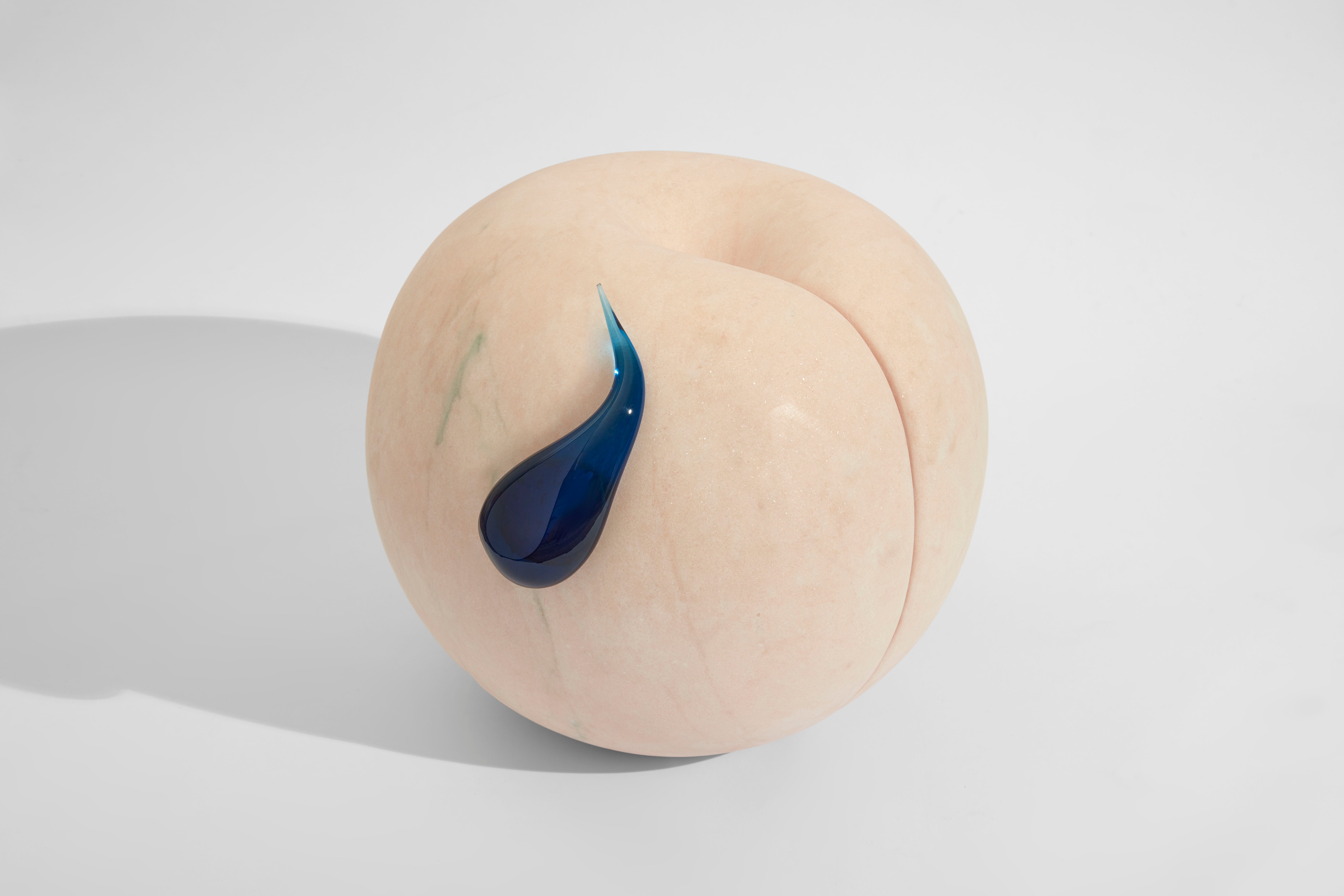 A round beige object that looks like a peach and has a blue glass tear drop on the side.
