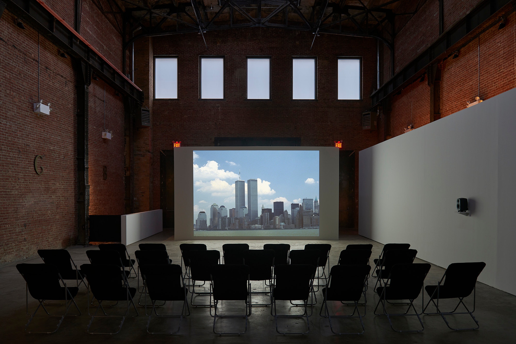 Three rows of black lawn chairs sit in front of a wall with a projected image of the World Trade Center.