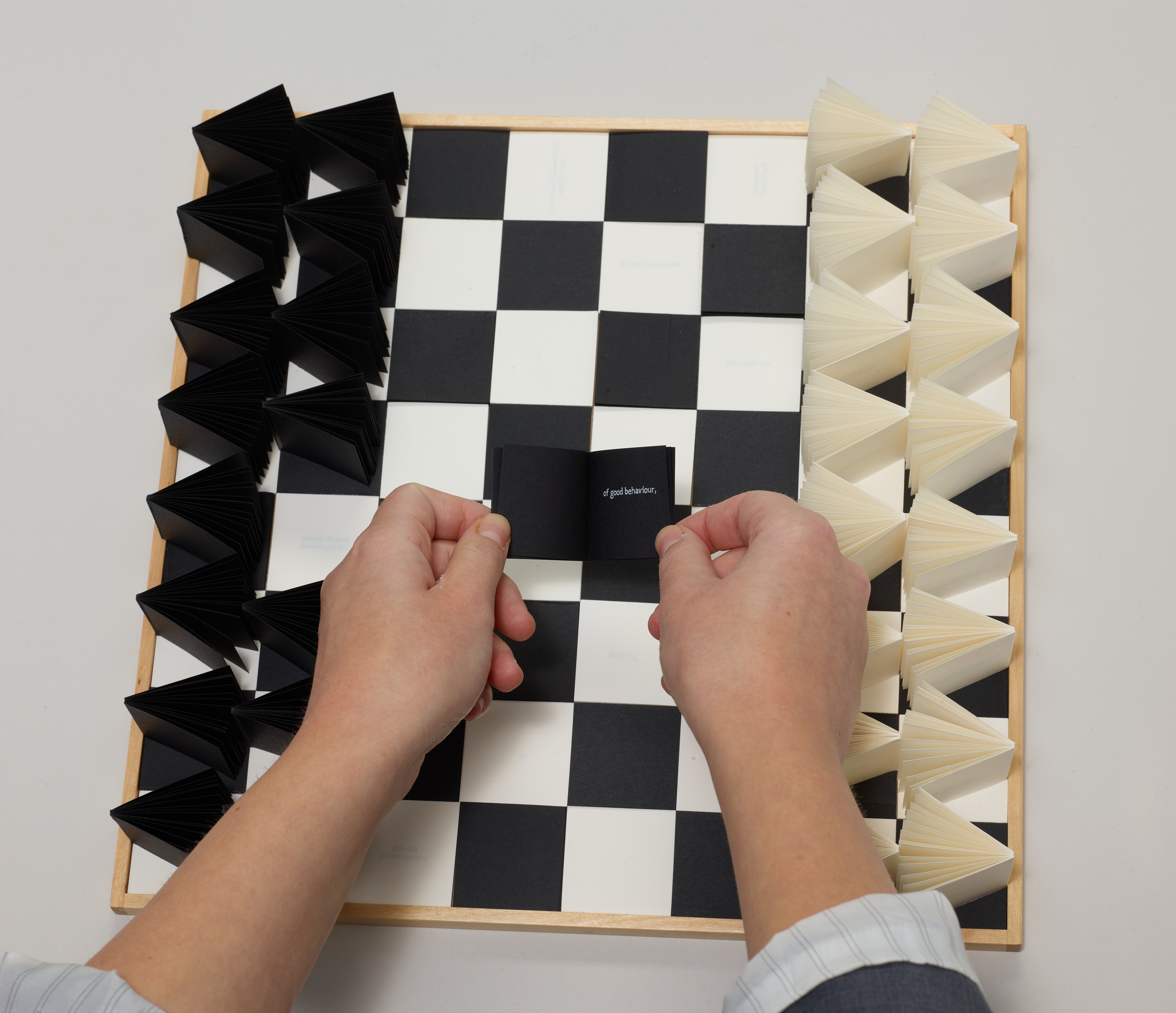 Light skin hands place a small book on a chess board.