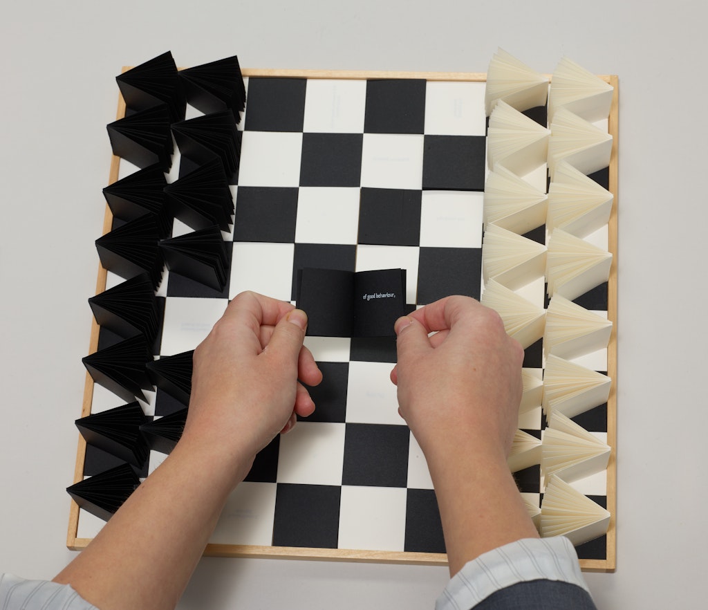 Light skin hands place a small book on a chess board.