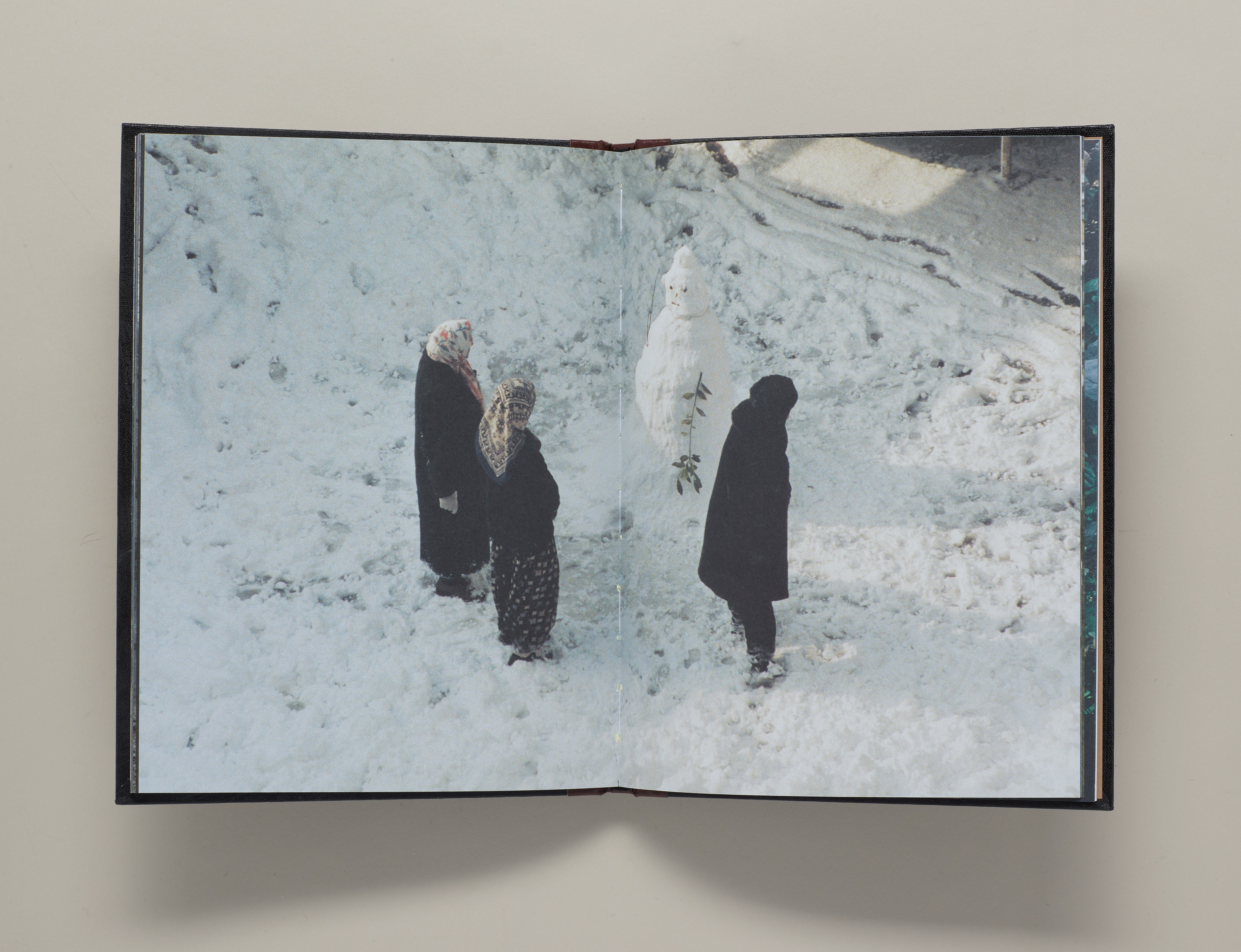 A book open to a page of three adults in scarves standing in snow and looking at a snowman.