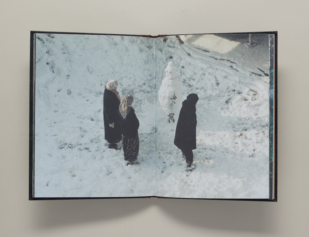 A book open to a page of three adults in scarves standing in snow and looking at a snowman.