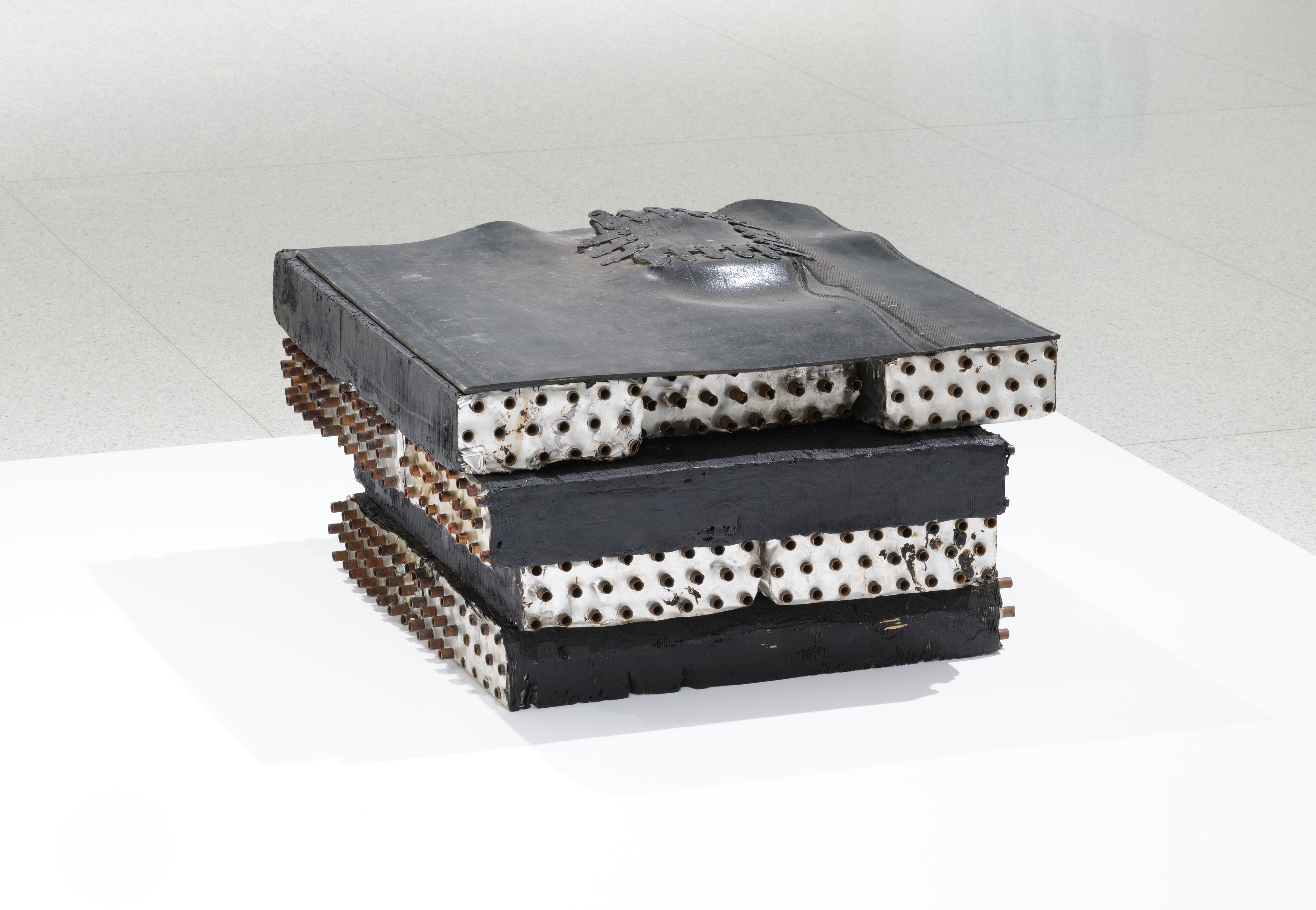 A object, mostly black, with rusty bolts on the side sits on a white surface.