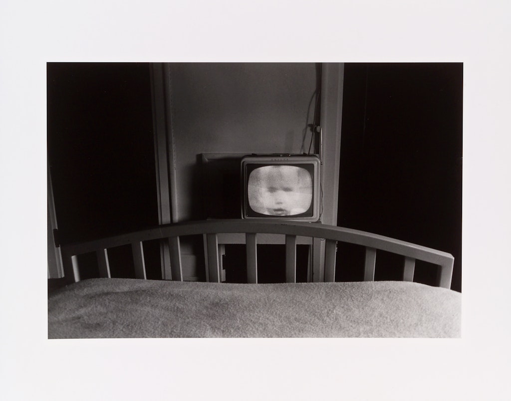 A black and white photo if a small tv at the end of a bed.