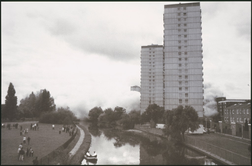 A black and white photo of a canal and tall buildings beside it.