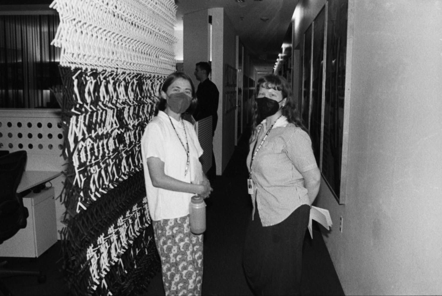 Two women wearing face masks stand and look at the viewer in the offices of a museum.