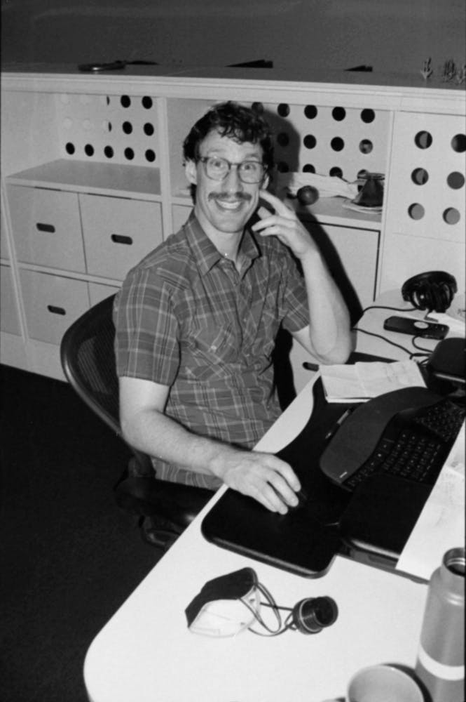 A man sits at a desk and smiles at the viewer in a museum office.