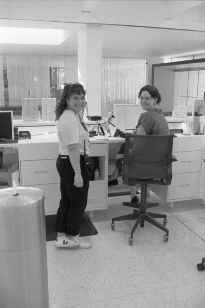 Two adults at a check in desk in a lobby turn around and smile at the viewer.