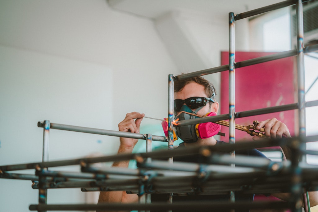 An adult wearing protective glasses and a mask welds metal structure