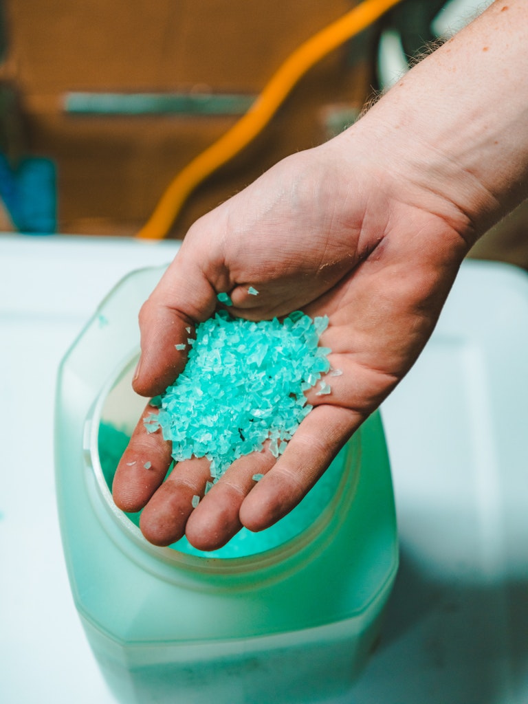 A robot arm 3D prints blue plastic fibers onto a circular form covered in tin foil on a table below.