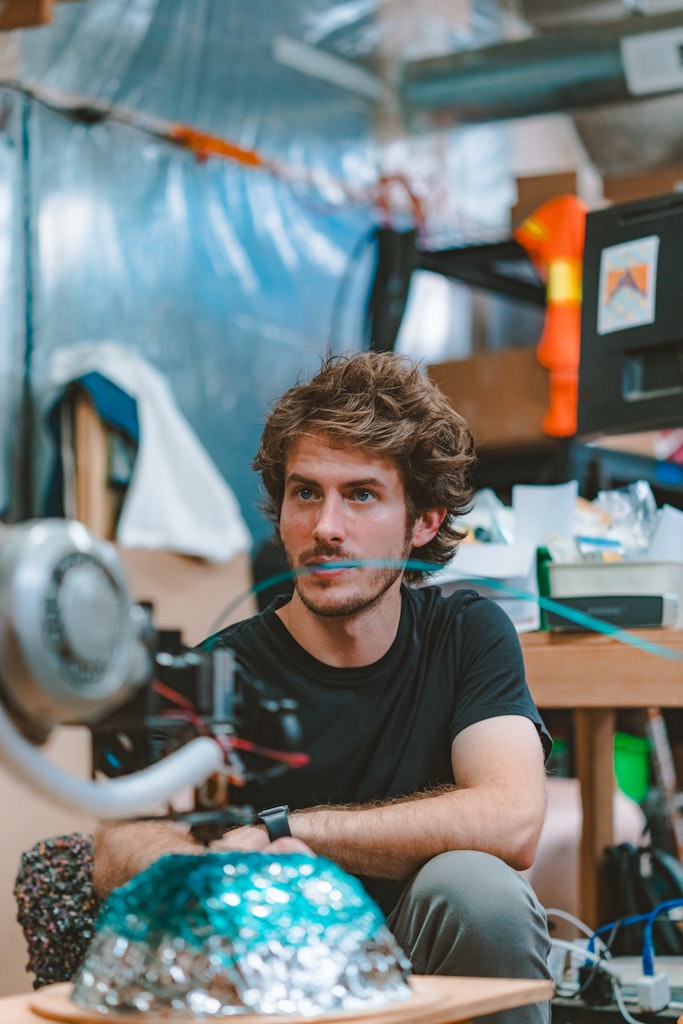 An adult with light skin looks at a plastic sculpture being formed.