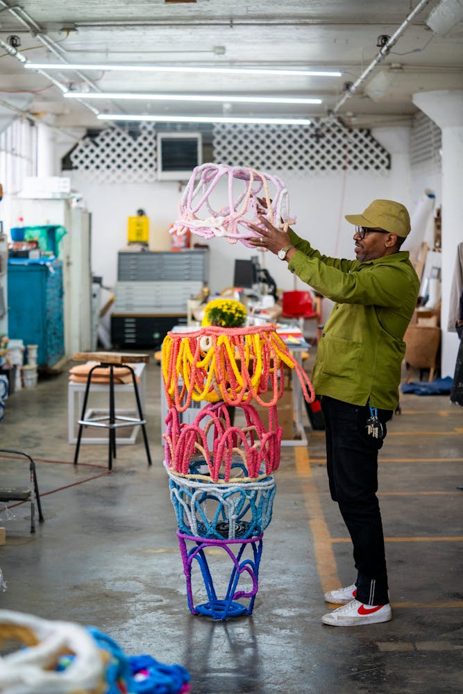 A man with dark skin plays with brightly colored sculpture in a studio.