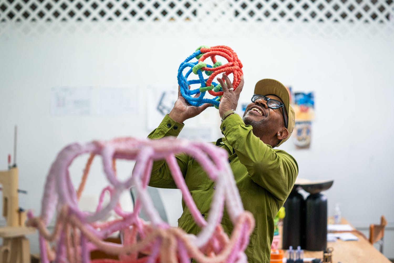 A man with dark skin plays with brightly colored sculpture in a studio.