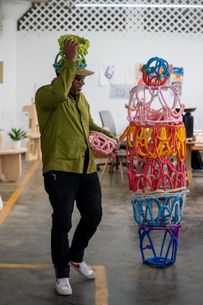 A man with dark skin plays with brightly colored sculpture in a studio.